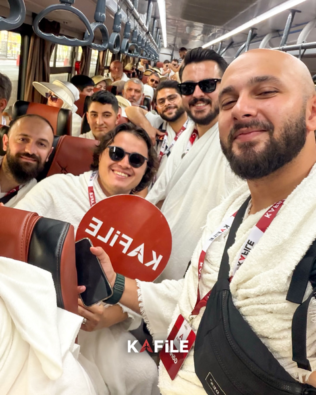 İhramlı Kafile Turizm misafirleri otobüste, Kafile tabelasıyla umre yolculuğunda